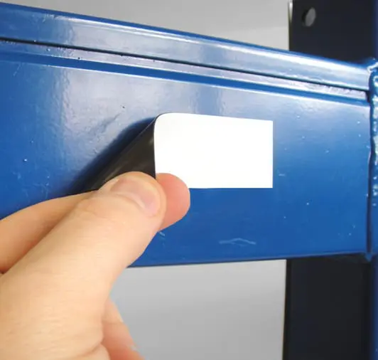 Hand peeling a white warehouse label from a blue metal surface.