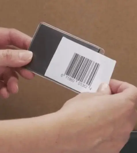 Hands placing a barcode into clear plastic label holders against a brown background.