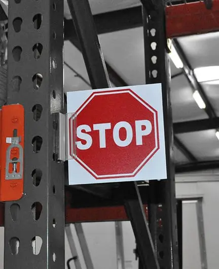 Small red stop sign on a metal frame, typical of branded warehouse signs in factories.