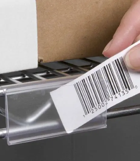 Hand sliding a barcode label into magnetic label holders on a metal shelf.