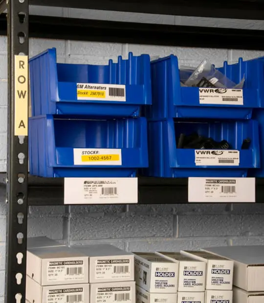 Blue storage bins with yellow labels in plastic label holders on a metal shelf marked ROW A.