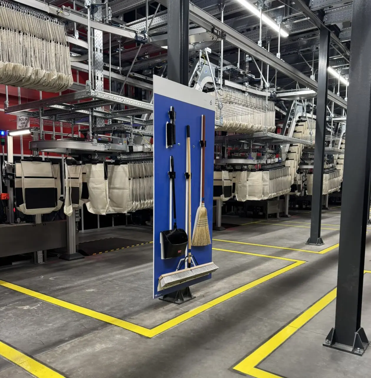 Cleaning tools on a blue board in a modern factory with conveyor belts and yellow floor lines.